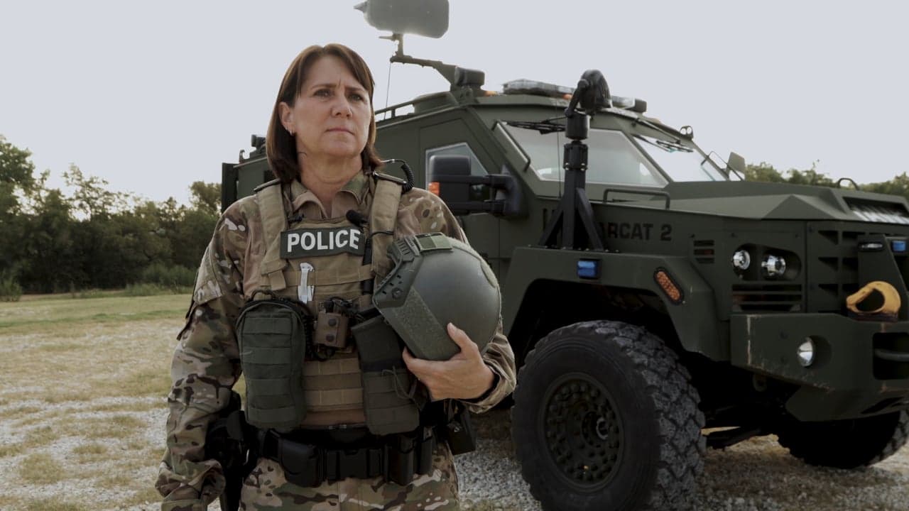 Police officer in multicam tactical gear and a POLICE vest standing in front of an olive BearCat armored vehicle