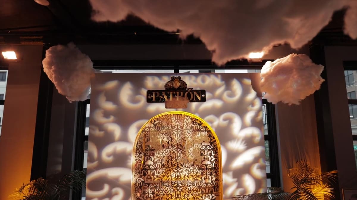Patron El Cielo Austin film still. Cloud sculptures and a gold Patron mark over an arched lattice.
